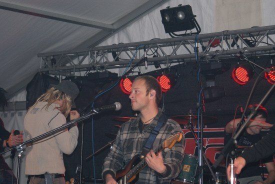 Eine Band spielt auf der Bühne mit roten Lichtern und einem Mikrofon. Der Leadgitarrist spielt eine Gitarre, während der Schlagzeuger Schlagzeug spielt.