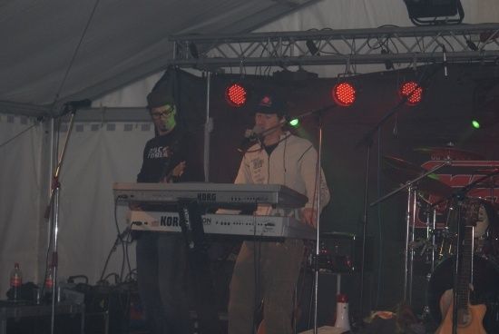 Zwei Männer spielen auf der Bühne mit einem Keyboard und Mikrofon unter roten Lichtern.