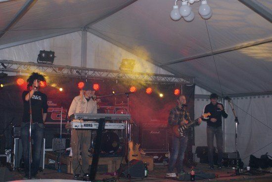 Eine Band spielt auf einer Bühne unter einem Zelt mit roter Beleuchtung und Mikrofonen.