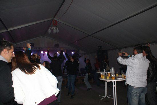 Eine Gruppe von Menschen tanzt und genießt eine Party unter einem Zelt mit lila Beleuchtung.