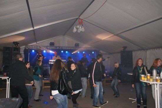Eine Gruppe von Menschen tanzt in einem Zelt mit Bühne, blauen Lichtern und Lautsprechern.