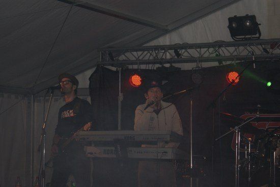 Zwei Männer spielen auf der Bühne mit einem Keyboard und einer Gitarre unter roten Lichtern.