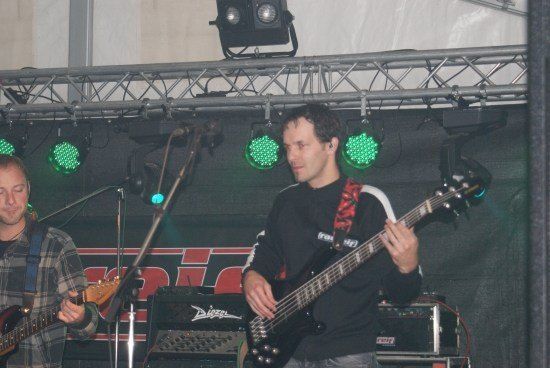 Zwei Männer spielen Gitarren auf der Bühne unter grünen Lichtern. Ein Mann trägt ein kariertes Hemd, der andere ein schwarzes Shirt.