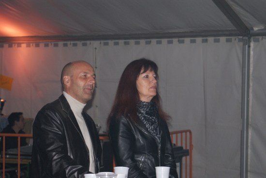 Ein Mann und eine Frau stehen gemeinsam in einem Zelt und schauen in die Kamera. Der Mann trägt eine Lederjacke und die Frau hat langes Haar. Sie halten beide Tassen.