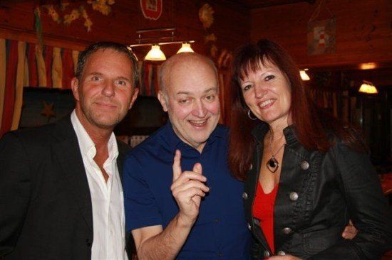 Drei Personen posieren für ein Foto in einem Restaurant. Der Mann in der Mitte macht ein Friedenszeichen.