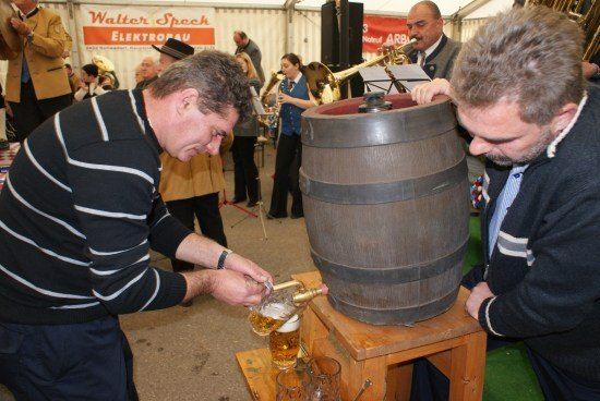 Zwei Männer schenken Bier aus einem großen Fass in Gläser. Eine Band spielt im Hintergrund.
