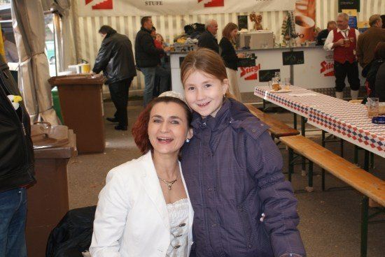 Eine Frau und ein junges Mädchen lächeln für ein Foto in einem Essenszelt mit anderen Leuten im Hintergrund.