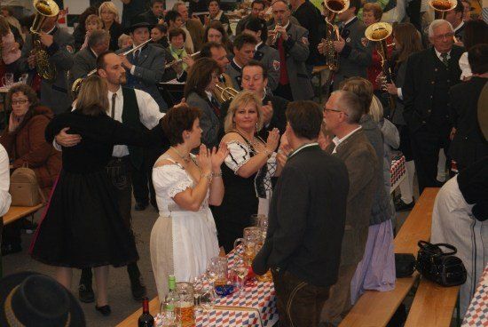 Eine lebhafte Zusammenkunft mit einer Band im Hintergrund, die spielt, Menschen tanzen und andere klatschen und jubeln. Eine Frau in einem weißen Kleid klatscht in die Hände.