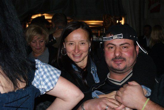 Ein Mann und eine Frau lächeln und posieren für ein Foto auf einer Party. Der Mann trägt eine schwarze Mütze und eine Uhr.