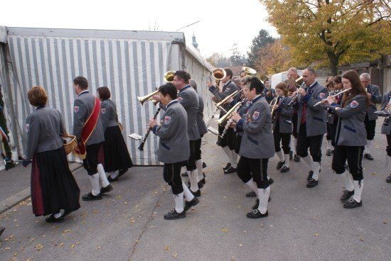 Eine Blaskapelle in traditionellen Uniformen spielt im Freien, wobei die Mitglieder verschiedene Instrumente wie Trompeten und Flöten spielen.
