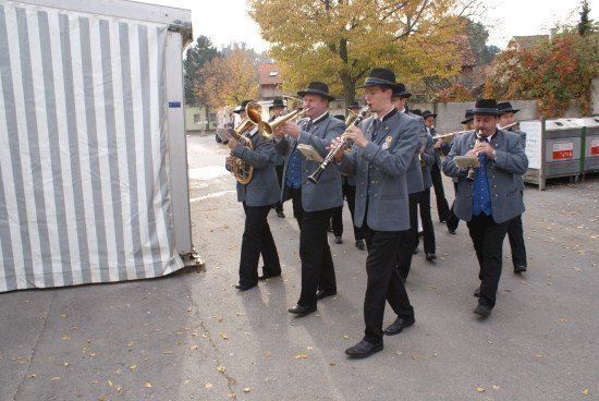 Eine Gruppe von Musikern in einheitlichen Kostümen spielt verschiedene Instrumente im Freien in einer städtischen Umgebung.