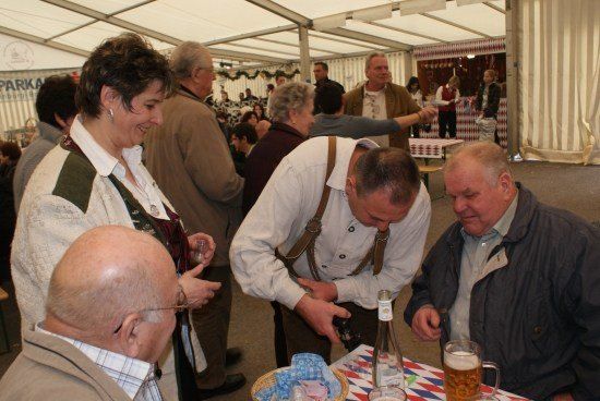 Eine Gruppe von Menschen in einem Zelt, zwei Männer öffnen eine Bierflasche, während andere zuschauen.