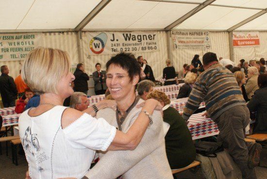Zwei Frauen tanzen in einem Zelt, während im Hintergrund eine Menschenmenge an Tischen sitzt.