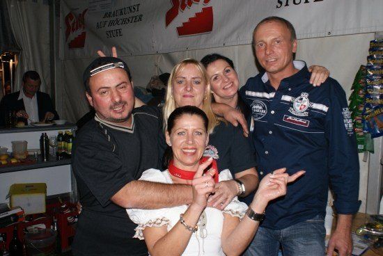 Fünf Menschen lächeln und posieren für ein Foto in einem Raum mit einem Banner und einigen Gegenständen auf einem Regal.