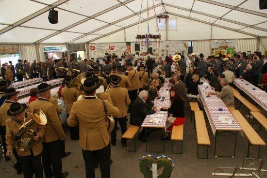 Eine große Gruppe von Menschen in Uniformen und Hüten versammelt sich in einem Zelt, einige spielen Instrumente und andere sitzen an Tischen.