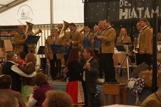Eine Band spielt auf der Bühne mit verschiedenen Instrumenten, während ein Paar vor ihnen tanzt und das Publikum zuschaut.