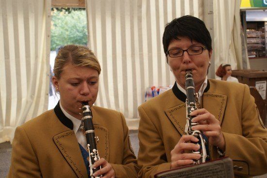 Zwei Frauen in braunen Uniformen spielen Klarinetten, eine liest Noten, in einem Zeltbereich.