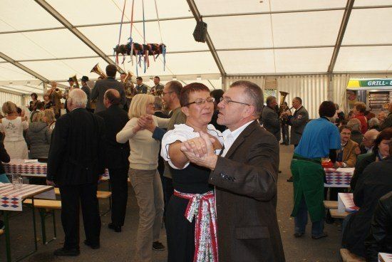 Ein Paar tanzt in einem Zelt-Event, während eine Brass-Band im Hintergrund spielt, umgeben von einer Menge.