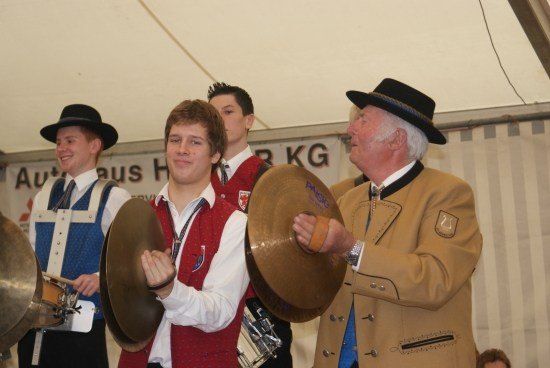Eine Gruppe von Männern in traditioneller Kleidung spielt Trommeln und Becken unter einem Zelt.
