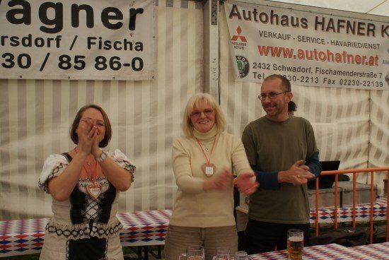 Drei Personen stehen vor einem Tisch mit Biergläsern. Zwei Frauen und ein Mann. Hinter ihnen sind Banner angebracht.