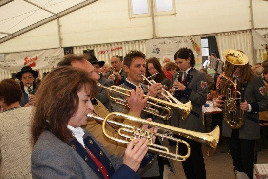 Eine Blechbläsergruppe spielt Trompeten und Tubas in einem Zelt, während eine Menschenmenge zuschaut.