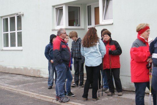 Eine Gruppe von Menschen in Winterkleidung steht vor einem Gebäude, möglicherweise warten sie auf etwas. Einige halten Skistöcke.