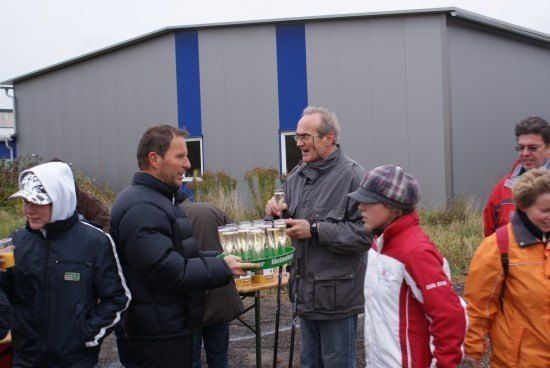 Eine Gruppe von Menschen, darunter zwei Männer, die ein Tablett mit Getränken halten, stehen vor einem Gebäude. Ein Mann lächelt und schaut in die Kamera.