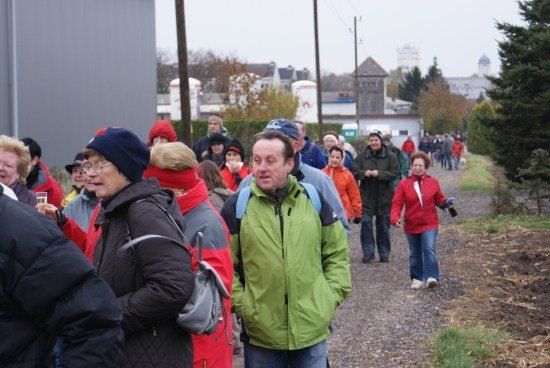 Eine Gruppe von Menschen in Winterkleidung geht einen Schotterweg entlang, mit Gebäuden und Bäumen im Hintergrund.