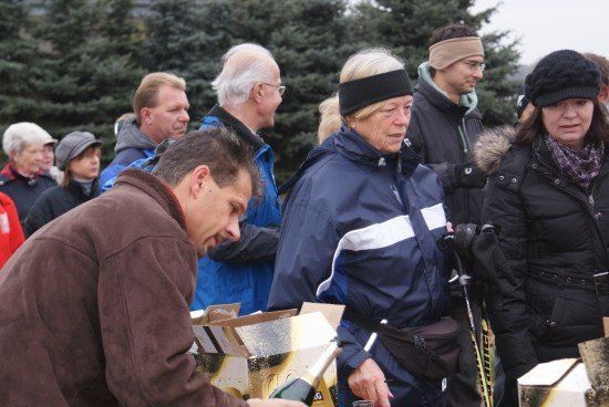 Eine Gruppe von Menschen im Freien, ein Mann öffnet eine Flasche Champagner, während andere zusehen, mit Tannenbäumen im Hintergrund.