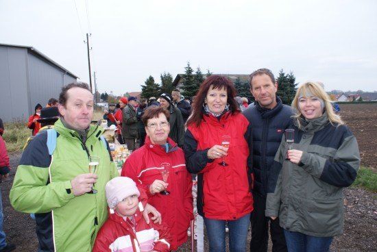 Eine Gruppe von Menschen in Wintermänteln und mit Weinläsern in der Hand steht in einem Außenbereich zusammen.