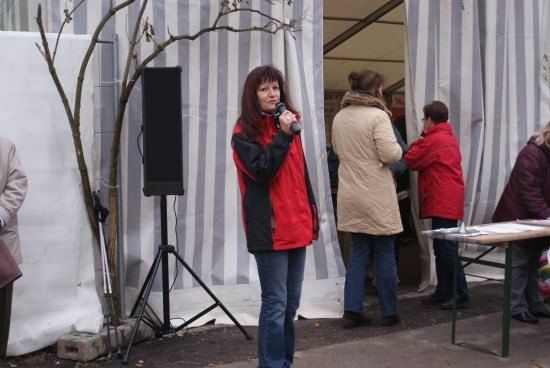 Eine Frau spricht in ein Mikrofon vor einem Zelt, mit Leuten in der Nähe.