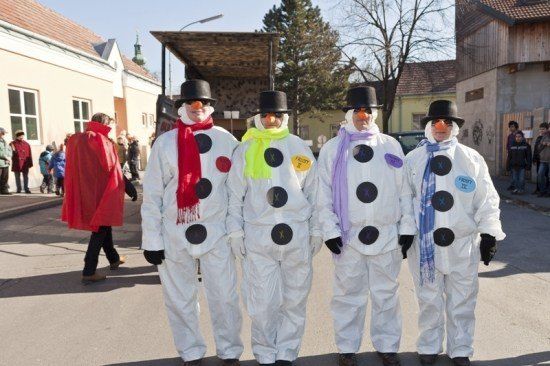 Vier Menschen, die als Schneemänner verkleidet sind, stehen in einer Reihe auf einer Straße, mit einer Menge Leute im Hintergrund.
