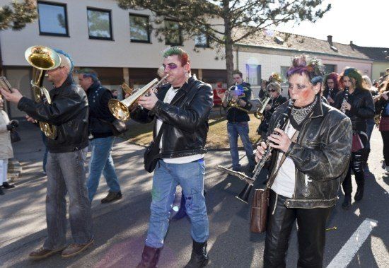 Eine Gruppe von Musikern in Lederjacken und Gesichtsbemalung spielt Blechblasinstrumente bei einer Straßenparade.