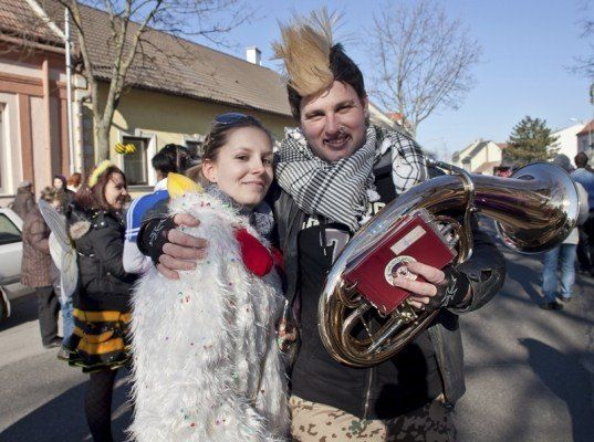 Ein Mann und eine Frau in Kostümen lächeln und posieren für ein Foto auf einer Straße mit anderen Menschen und Gebäuden im Hintergrund.