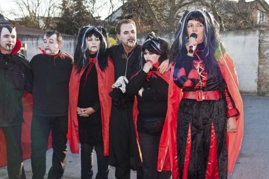 Eine Gruppe von Menschen in Vampirkostümen posiert für ein Foto, wobei eine Frau ein Mikrofon hält.