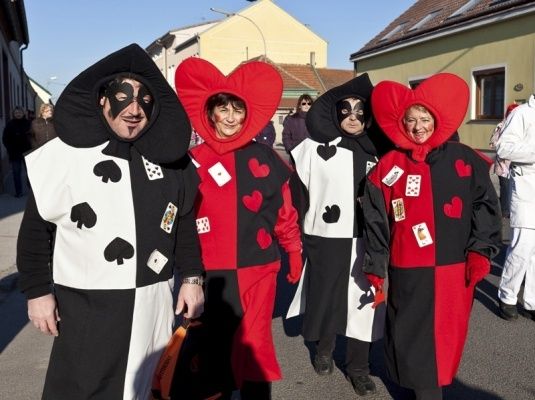 Vier Menschen in Kostümen gehen die Straße entlang, jeder trägt einen herzförmigen Hut und eine Gesichtsmaske. Die Kostüme sind schwarz und rot mit Spielkartendesigns.