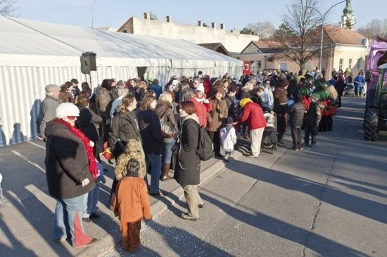 Eine Menschenmenge steht in einer Schlange vor einem weißen Zelt auf einer Straße, mit Gebäuden und Bäumen im Hintergrund.