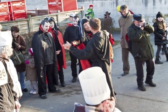 Eine Gruppe von Menschen in Kostümen, darunter einige in Vampir-Aufmachung, versammelt sich im Freien, wahrscheinlich für eine Halloween-Veranstaltung. Eine Person macht ein Foto, während andere interagieren.