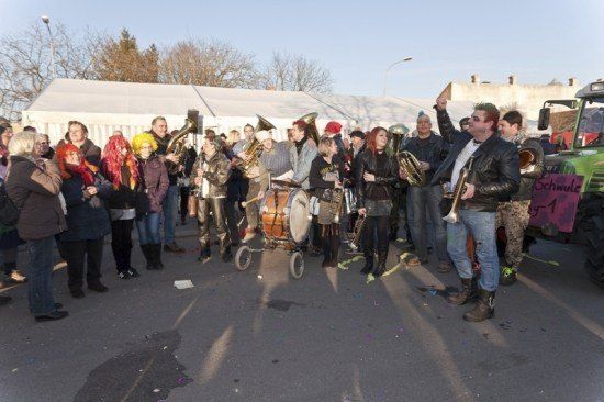 Eine Gruppe von Menschen in Kostümen und Lederjacken spielt mit Blechblasinstrumenten und Trommeln in einem Freiluftbereich.