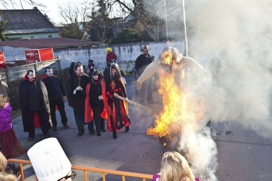 Eine Gruppe von Menschen in Kostümen verbrennt eine Puppe auf der Straße. Die Puppe steht in Flammen und ist von Rauch umgeben.
