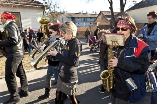 Eine Gruppe von Musikern, darunter eine Frau mit einer Saxophon und ein Mann mit einer Tuba, spielen auf einer Straße, während eine Menge zuschaut.