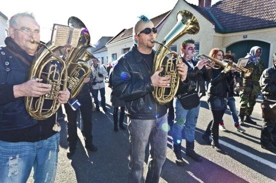 Eine Gruppe von Musikern, einige in Freizeitkleidung und andere in Militäruniformen, spielen Blechblasinstrumente im Freien.