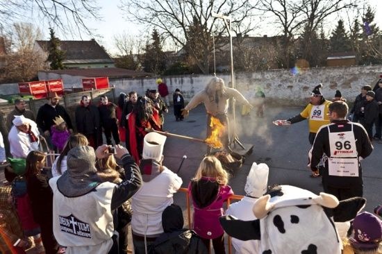 Eine Menschenmenge in Kostümen und Hüten versammelt sich um einen Mann in Flammen, der auf einer Straße steht.