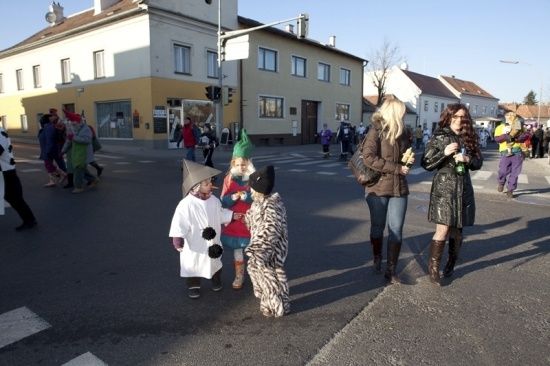 Eine Gruppe von Menschen, einschließlich Kinder in Kostümen, gehen auf einer Straße während eines Umzugs. Gebäude säumen die Straße, und einige Leute stehen auf dem Bürgersteig.