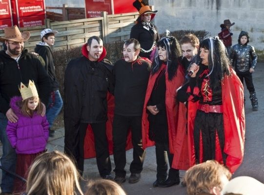 Eine Gruppe von Menschen in Halloween-Kostümen, darunter Dracula und eine Hexe, steht vor einer Menge.
