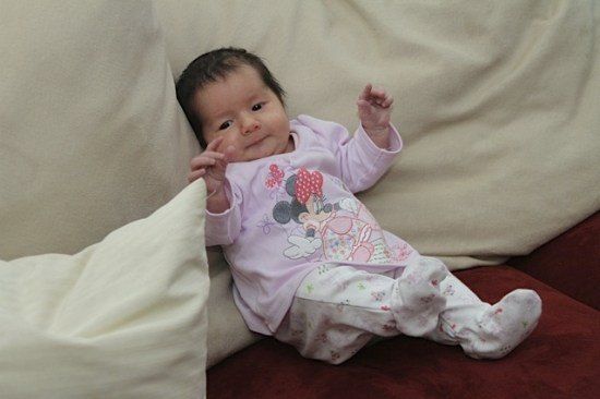 Ein Babymädchen in rosa Minnie-Mouse-Pyjamas liegt auf einem Sofa, lächelt und schaut in die Kamera.