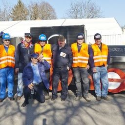 Eine Gruppe von Männern in Sicherheitswesten und Mützen posiert vor einer großen, farbenfrohen zugähnlichen Struktur.