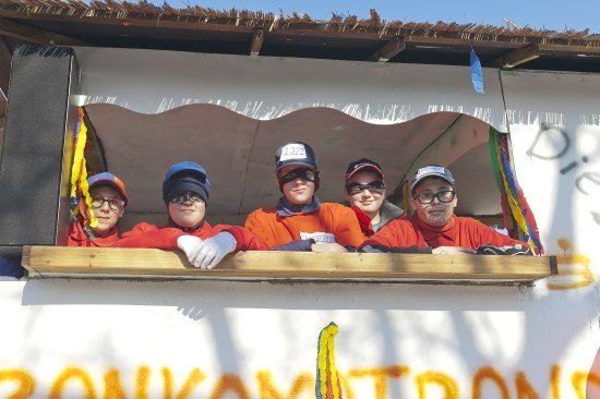 Eine Gruppe von Menschen in orangefarbenen Hemden und Mützen posiert für ein Foto in einer dekorierten Kabine.