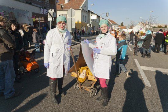 Zwei Frauen, die als Ärzte verkleidet sind, schieben einen Wagen mit einer Puppe darauf auf einer belebten Straße.
