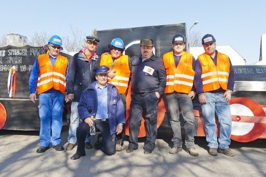 Eine Gruppe von Männern in Sicherheitsausrüstung posiert für ein Foto vor einem großen schwarzen Hintergrund mit Graffiti und einem roten und weißen Schild.